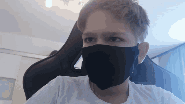 a young man wearing a black face mask looks at the camera