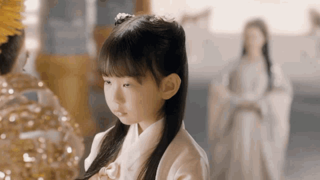a little girl in a white dress is looking at something in a room