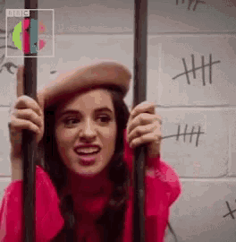 a woman in a pink hat is behind bars with a bbc logo behind her