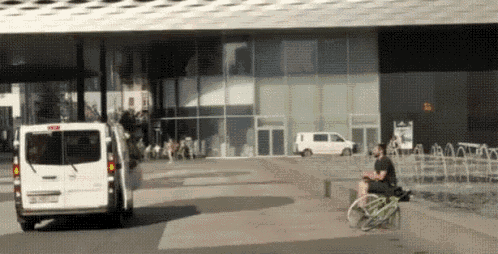 a white van is driving past a man riding a bike in front of a building