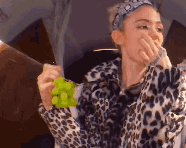 a woman in a leopard print jacket holds a bunch of grapes