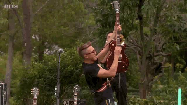 a man playing a guitar with bbc written on the bottom right