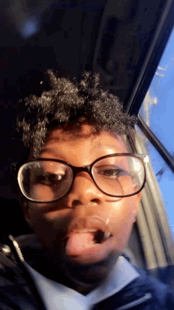 a boy wearing glasses is sticking his tongue out