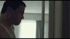 a man in a white tank top is standing in front of a mirror in a room .