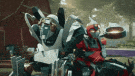 a couple of robots standing next to each other in front of a red barn .