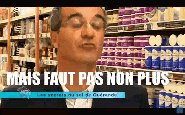 a man in a suit stands in front of a shelf of toilet paper that says " mais faut pas non plus " on it