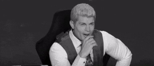 a man in a suit and tie is sitting in a chair with his mouth open and his hands folded .