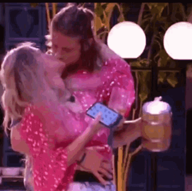 a man is holding a woman in his arms while she holds a cell phone and a beer mug .