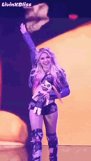 a woman in a wrestling outfit is holding a stuffed animal and waving .