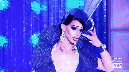 a drag queen is holding a feather in her hand while standing on a stage .