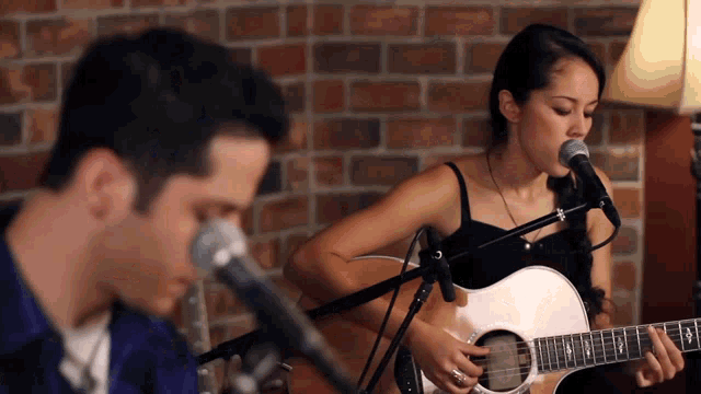 a woman singing into a microphone while a man plays guitar