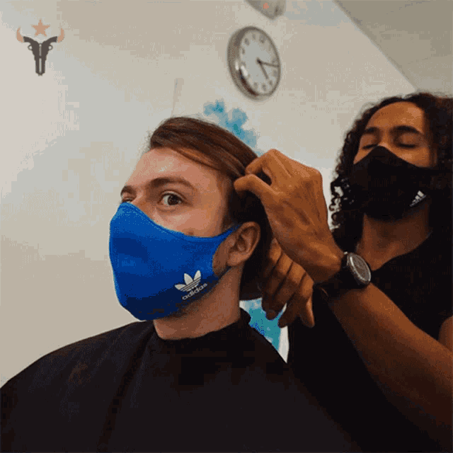 a man wearing a blue adidas face mask is getting a haircut