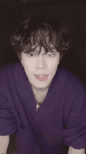 a young man with curly hair wearing a purple sweater