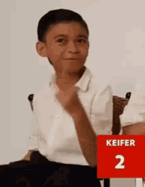 a young boy sitting in a chair with a red sign that says keifer 2 on it