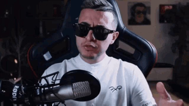 a man wearing sunglasses is sitting in front of a rode brand microphone