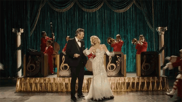 a man in a tuxedo and a woman in a white dress are dancing on a stage in front of a band