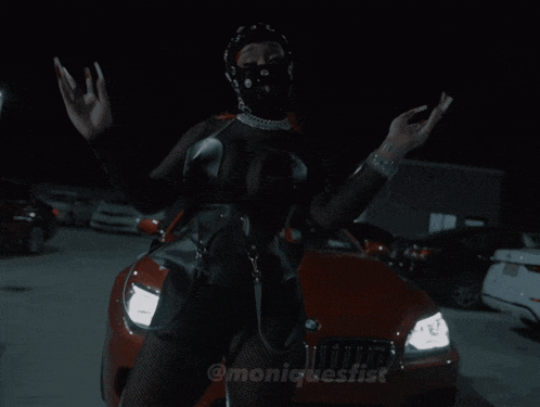 a woman in a black outfit is standing in front of a red car with the name moniqbestist on the bottom