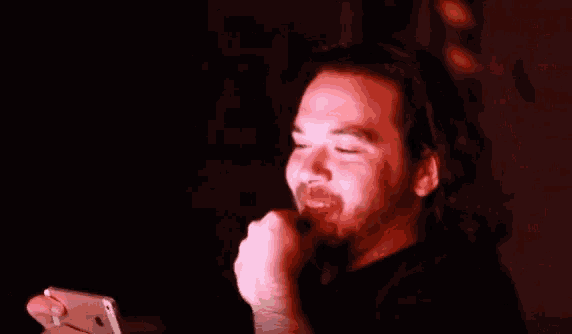 a man with long hair and a beard looks at his phone in the dark