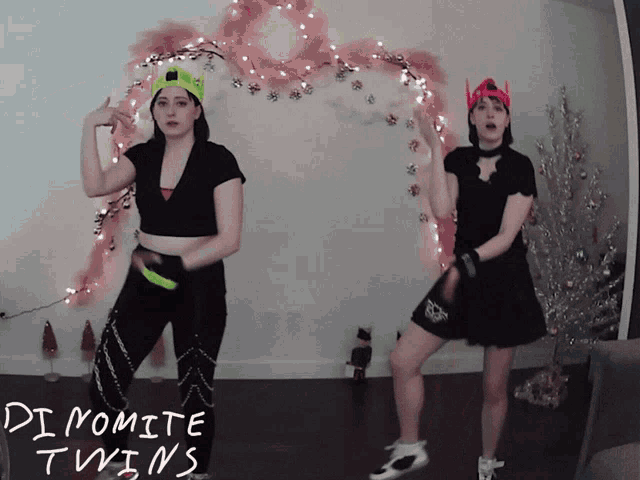 two women are dancing in front of a christmas tree with the words dynamite twins on the bottom