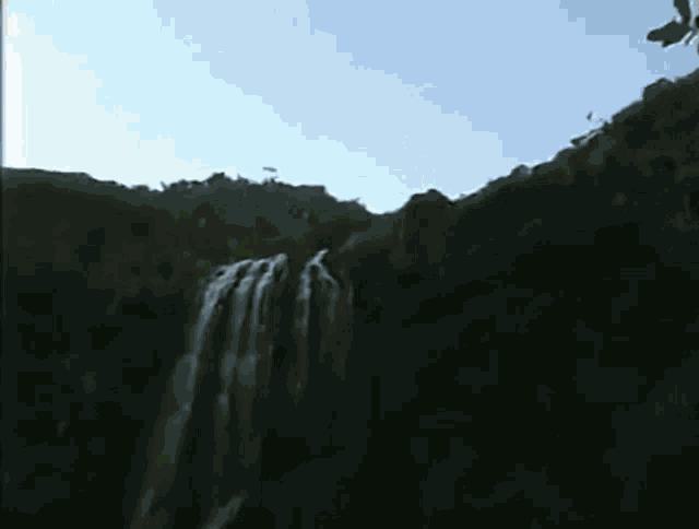 a waterfall in the middle of a dark forest with a blue sky in the background