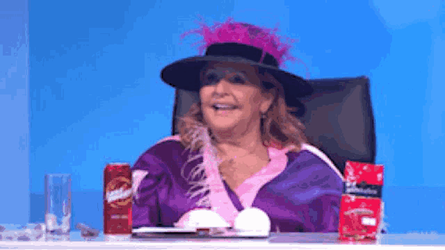 a woman wearing a purple dress and a black hat sits at a table with a can of budweiser