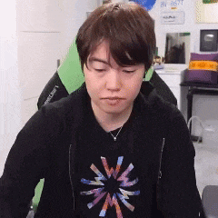a young man is sitting in a chair wearing a black shirt with a colorful star on it .