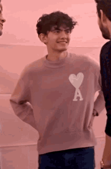 a young man wearing a pink sweater with a white heart and the letter a on it