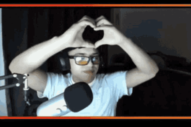 a man wearing glasses is making a heart shape with his hands in front of a microphone