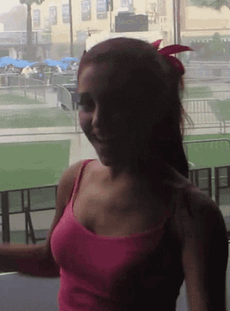a woman in a pink tank top with a red bow in her hair is smiling