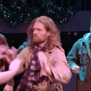 a man with long hair and a beard is wearing a trench coat and a scarf .