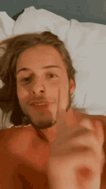 a man with long hair and a beard is laying on a bed and giving a thumbs up