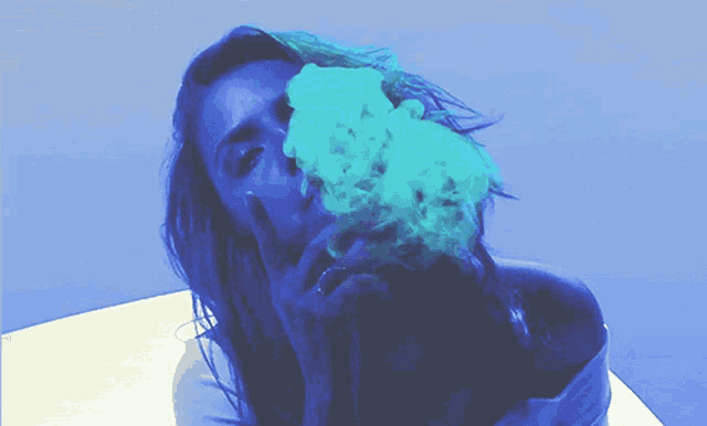a woman blowing blue smoke from her mouth while giving the middle finger