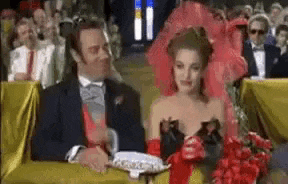 a man and a woman are sitting at a table in front of a crowd at a wedding ceremony .