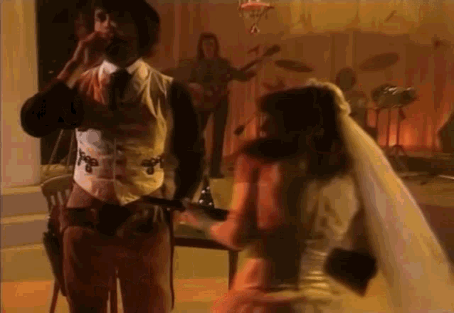 a man in a suit and tie is standing next to a woman in a veil playing a guitar .