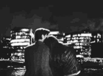 a black and white photo of a man and a woman looking at a city at night