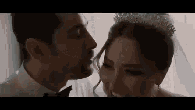 a bride and groom are kissing in front of a window .