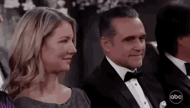 a man in a tuxedo and a woman in a dress are sitting next to each other at a wedding reception .