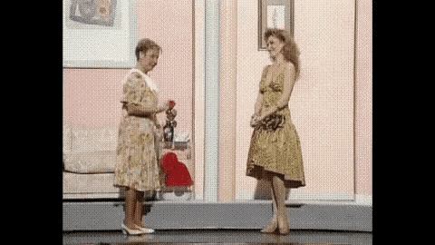 two women in dresses are standing next to each other on a stage in front of a pink wall .
