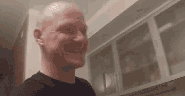 a bald man is smiling in a kitchen while standing in front of cabinets .