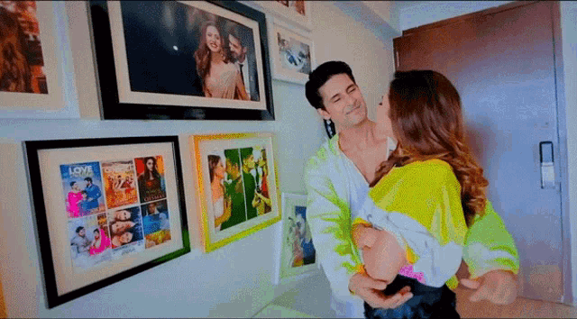 a man holds a woman in his arms in front of a wall of framed pictures including one that says love on it