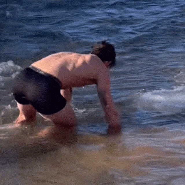 a shirtless man in black shorts is kneeling in the water