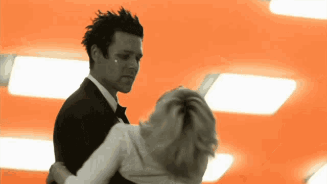 a man in a tuxedo is dancing with a woman in a white shirt