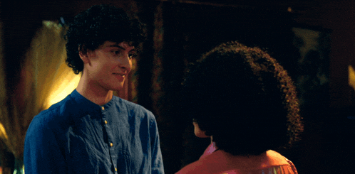 a woman with curly hair is smiling at a man in a blue shirt