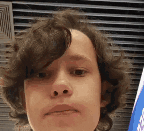 a young man with curly hair is making a funny face in front of a sign .