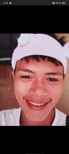 a young man wearing a pink headband with white ears smiles for the camera