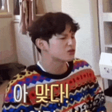 a young man in a colorful sweater is making a funny face in a room .