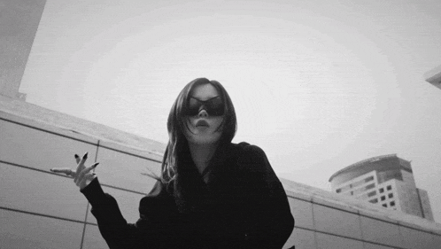 a black and white photo of a woman wearing sunglasses making a peace sign