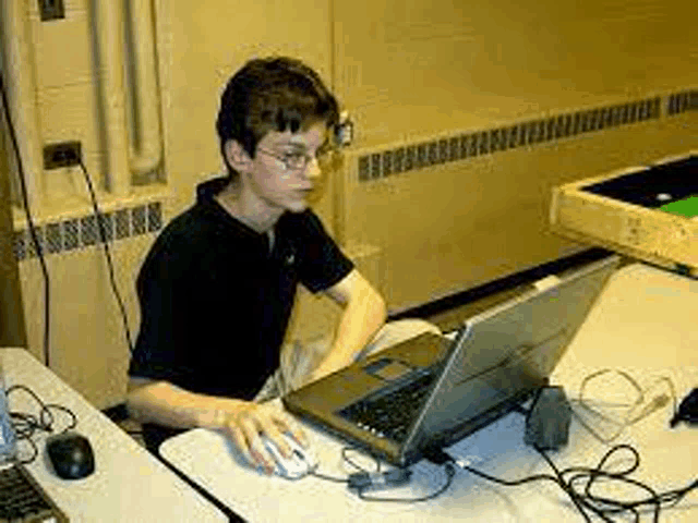 a young man is sitting at a table with a laptop and a mouse .