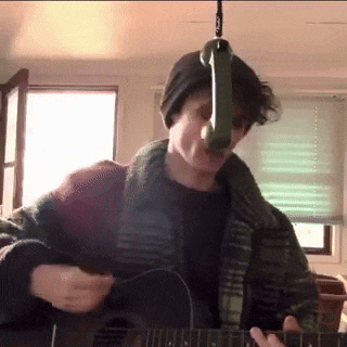 a man playing an acoustic guitar with a microphone hanging from the ceiling