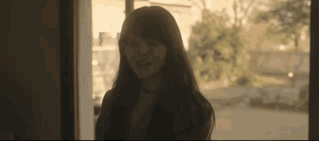 a young woman with long hair is standing in front of a window .